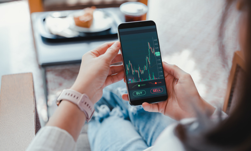 Hand holding a phone showing an investment graph with a mobile phone investing application