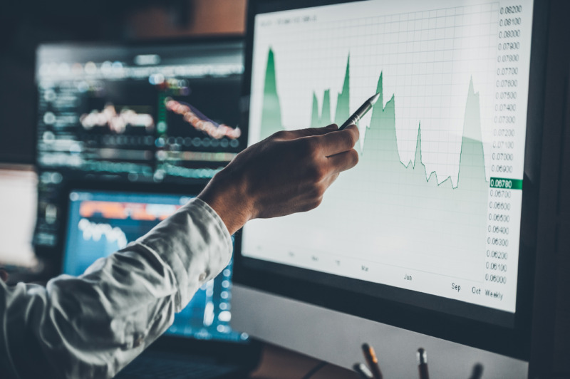 Hand pointing an investment graph and data on a computer monitor