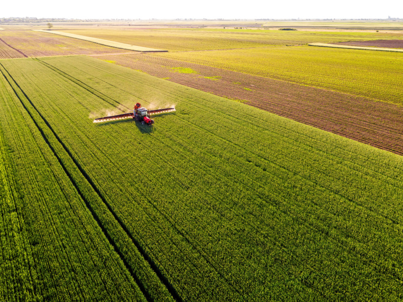 Aerial view of a red tractor treating wheat crops across huge farmland