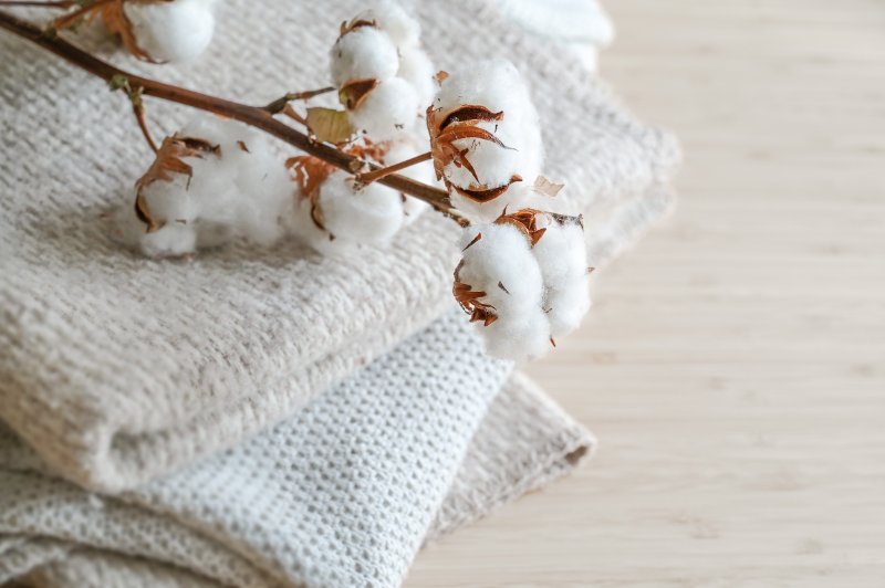 Branch with fluffy cotton balls on a pile of natural colored fabrics