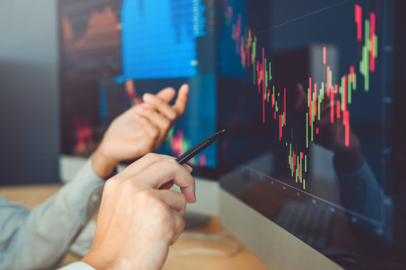 Hands pointing at and discussing a stock market trading graph, analyzing the data and trends